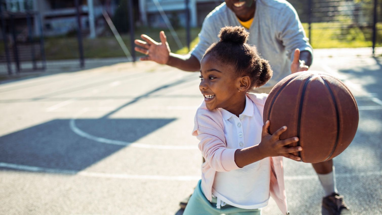 Dad plays basketball outside with daughter